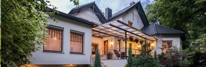 A large white house with a large porch is surrounded by trees.