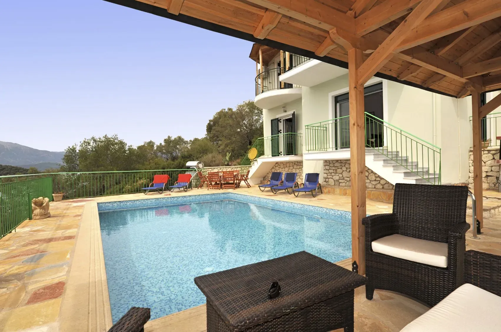 A large swimming pool is surrounded by wicker furniture