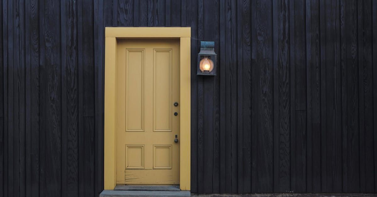 A yellow door is on a black wooden wall next to a lantern.