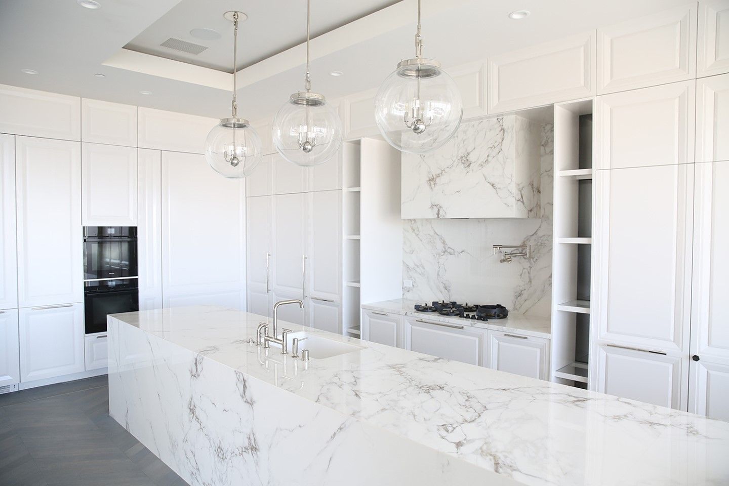 Bright white luxury kitchen with marble island, glossy cabinets, and pendant lights