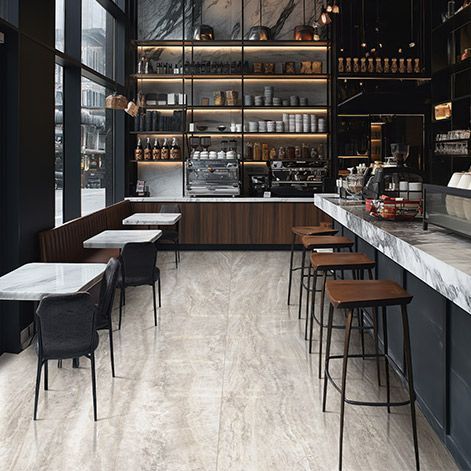 Modern cafe interior with marble tables, bar stools, and shelves of bottles behind the counter