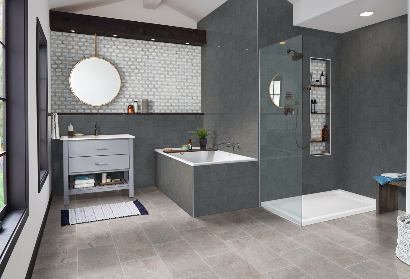 Modern bathroom with gray tile, walk-in glass shower, floating vanity, and round mirror