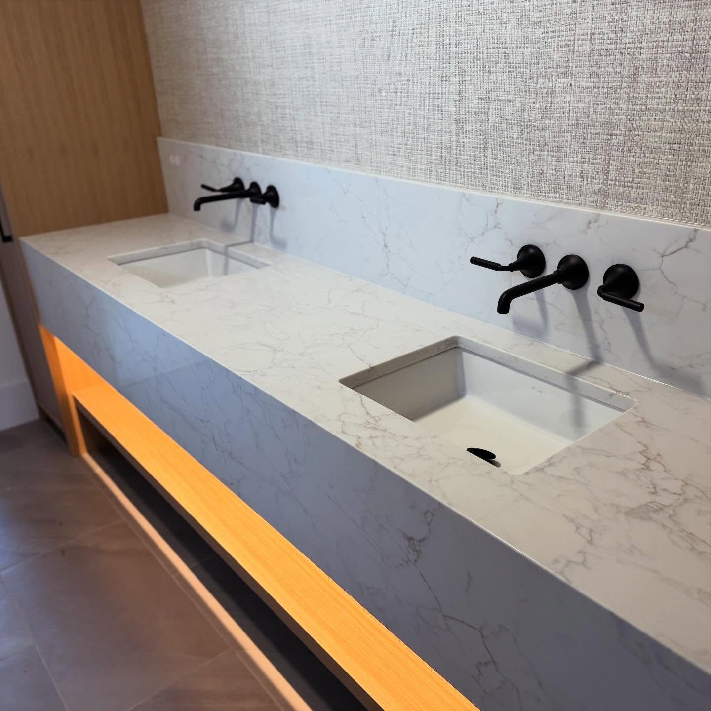 Modern restroom with two marble sinks, black faucets, and orange underlighting