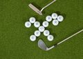 Golf balls arranged in an X shape on green turf with a putter and wedge.