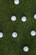 Golf balls arranged in an X shape on green turf with a putter and wedge.