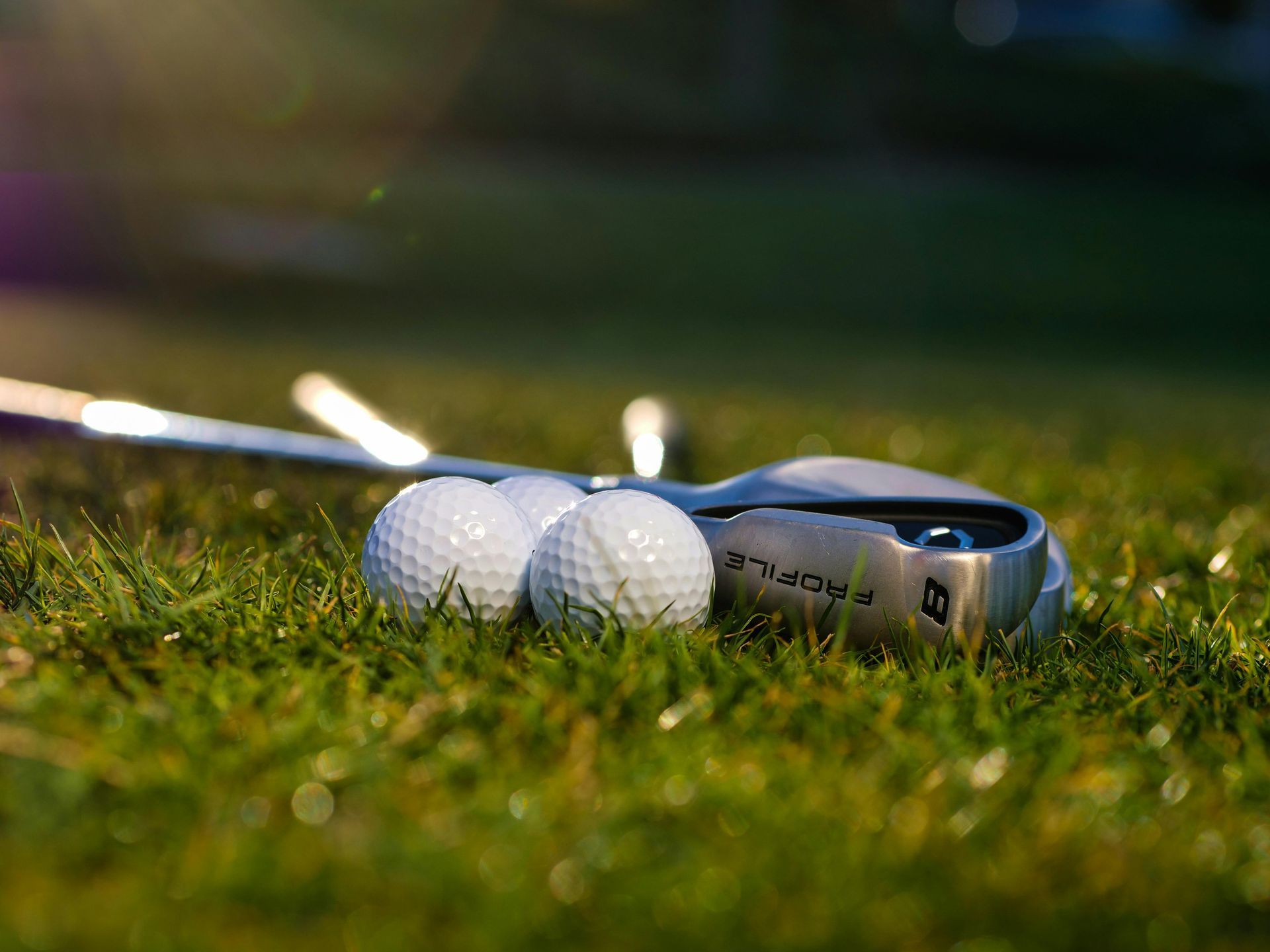 Person wearing a white hat lies on green grass, surrounded by golf balls, with a golf club nearby.