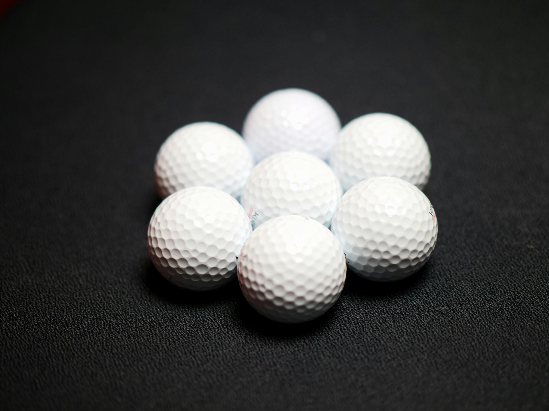 Seven white golf balls arranged in a circle on a dark textured surface.