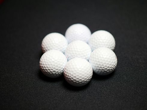 Seven white golf balls arranged in a circle on a dark textured surface.