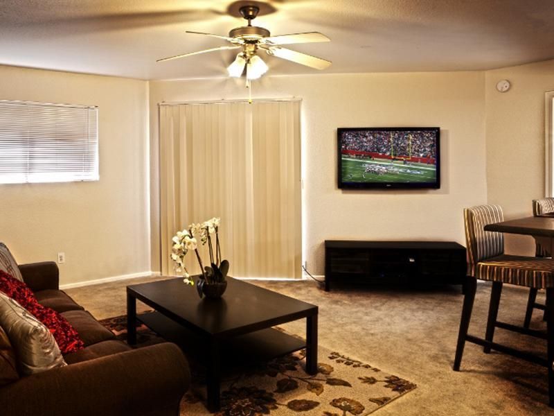 A living room with a ceiling fan and a flat screen tv on the wall.