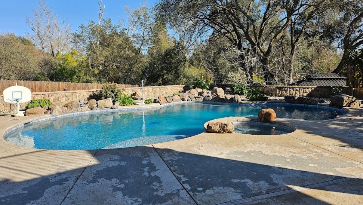 A large swimming pool surrounded by trees and a basketball hoop.