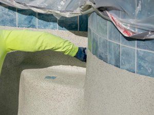 A man in a yellow jacket is working on a swimming pool.