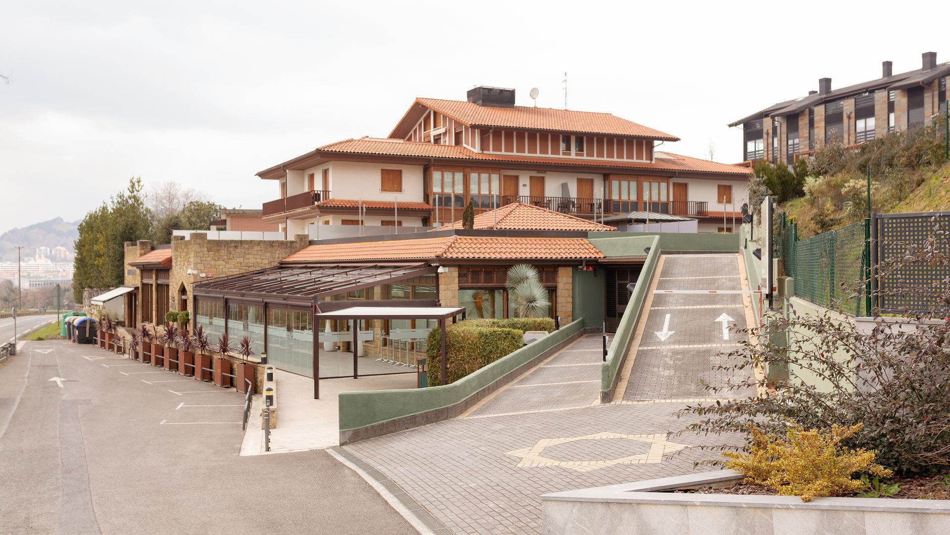 Zarautz escuela cocina, con techo de tejas rojas, exterior de piedra y vidrio, entrada para vehículos, pérgola