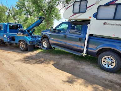 A blue truck with a camper on top of it is being towed by a tow truck.