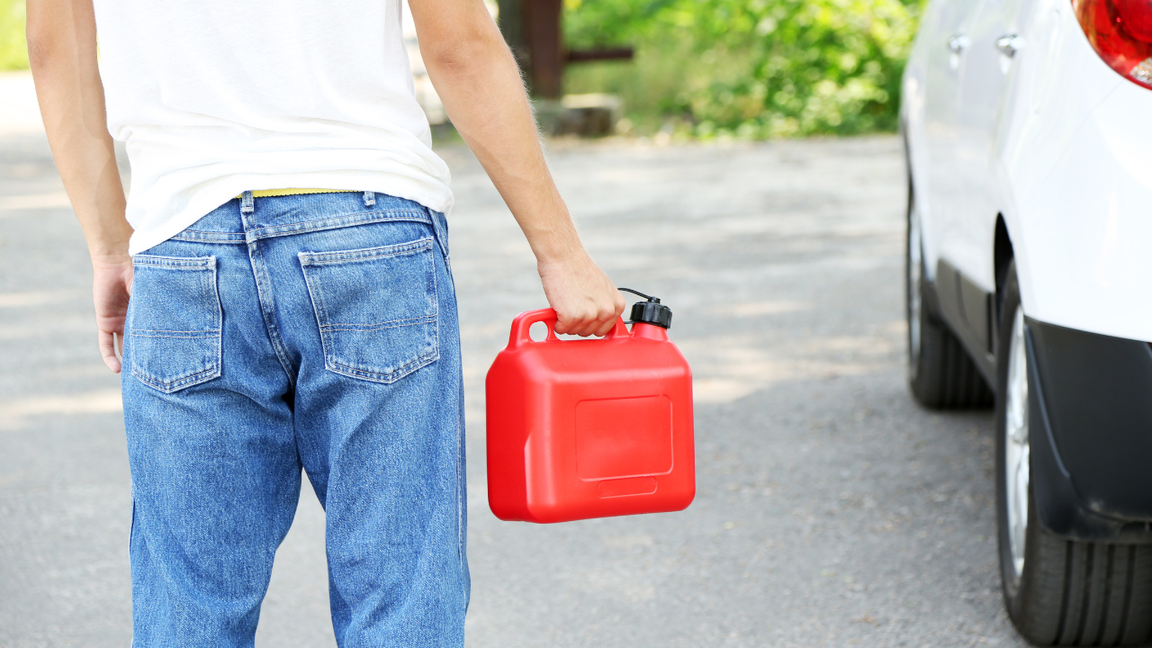 A man is holding a red gas can in front of a car.