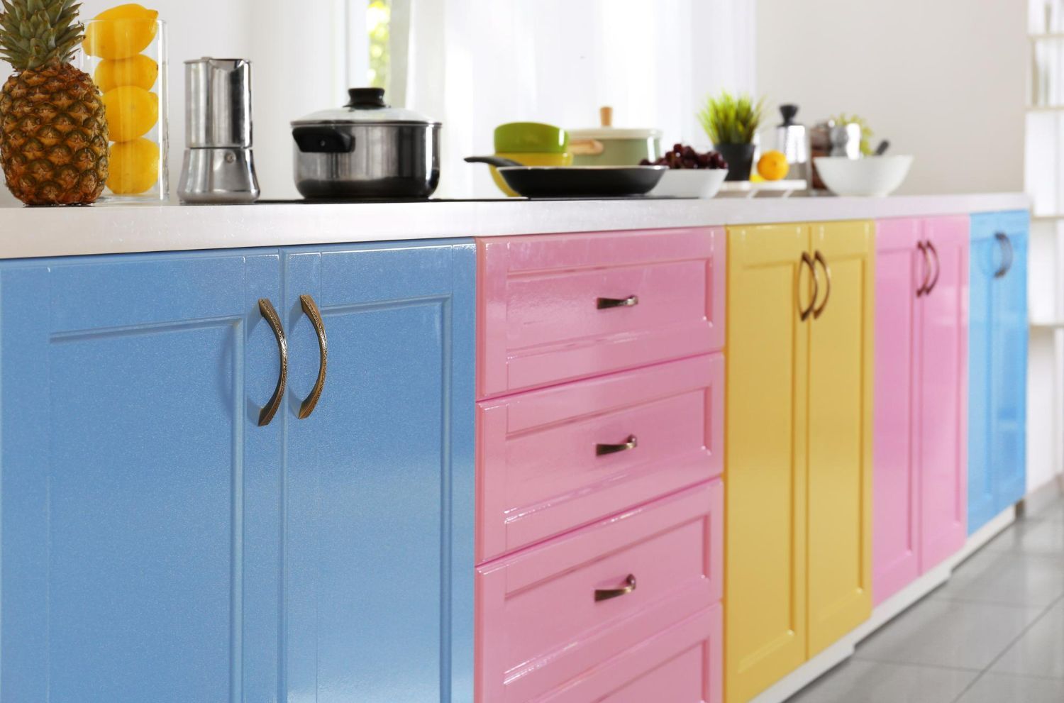 A kitchen with colorful cabinets and drawers and a pineapple on the counter.