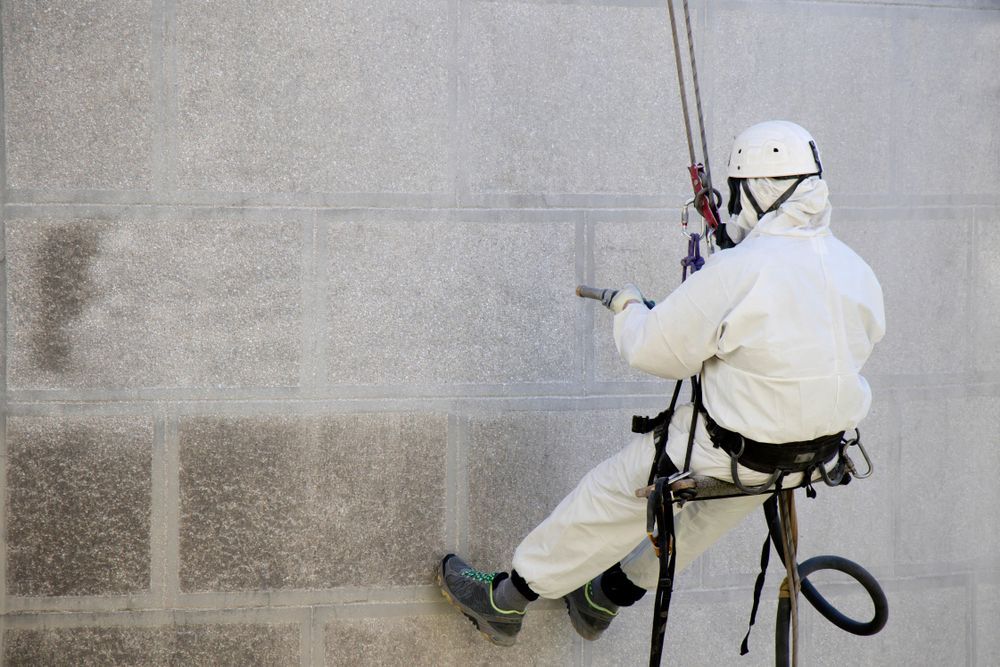 A man in a white suit is cleaning a wall with a hose.