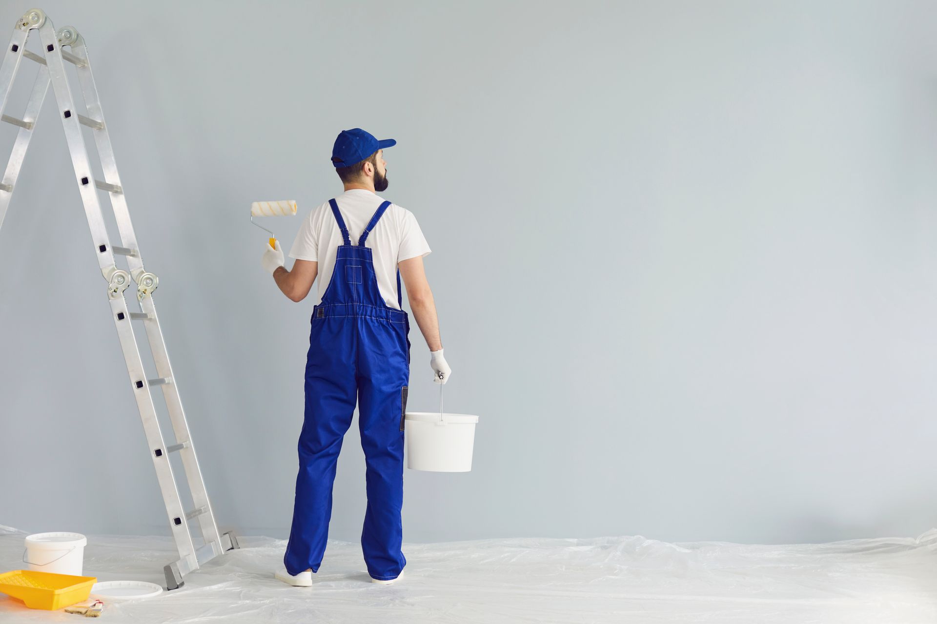 A man is painting a wall with a roller and bucket.