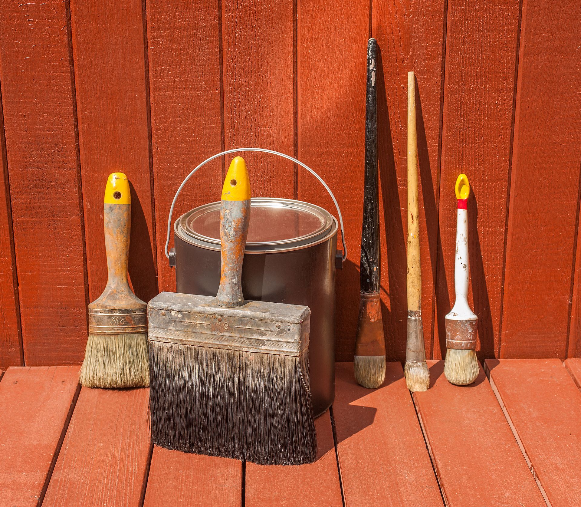 A bucket of paint and brushes on a wooden deck