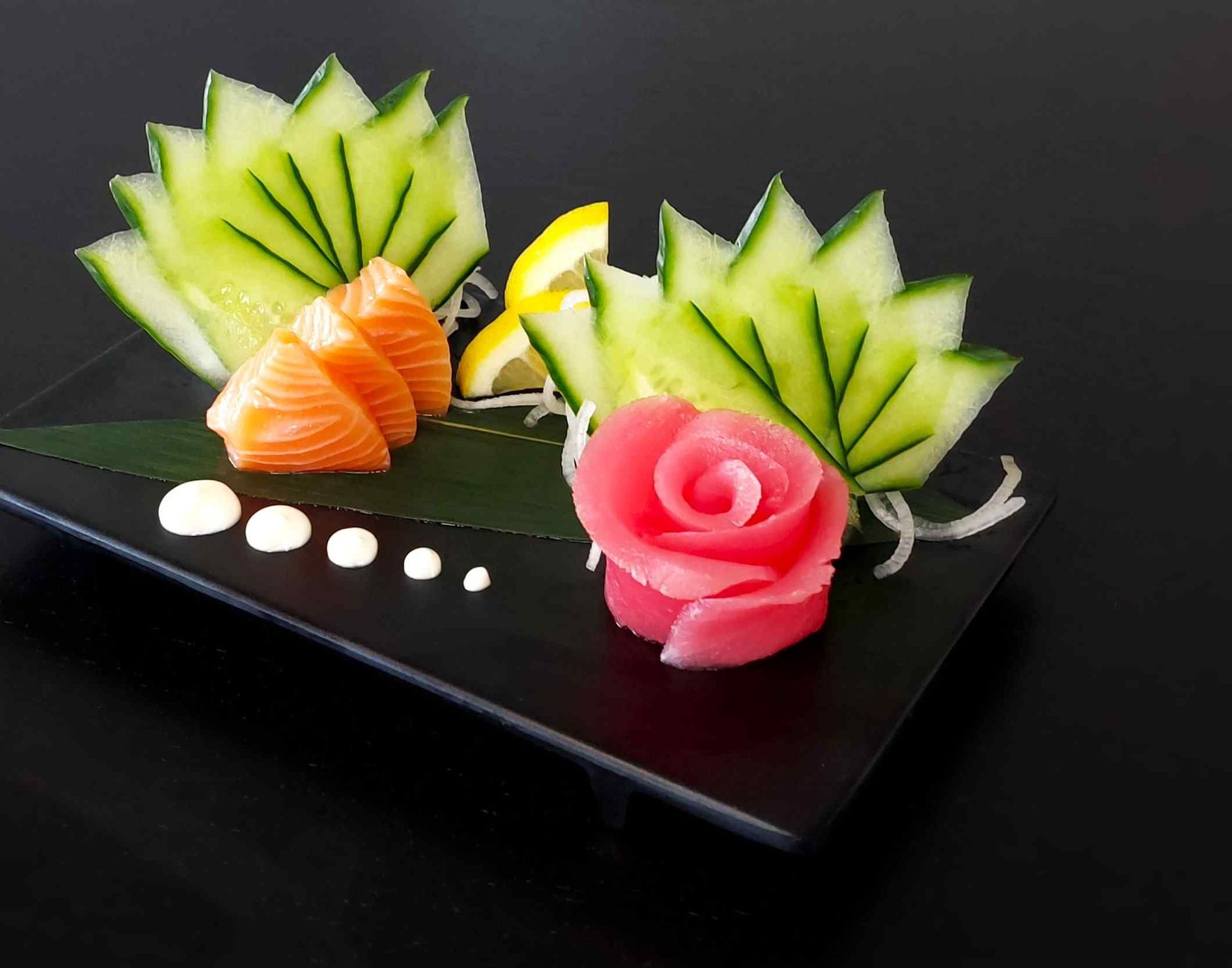 A black plate topped with sliced vegetables and a pink rose