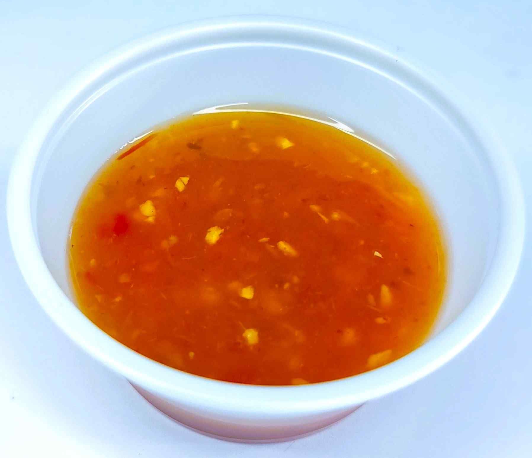 A plastic cup filled with orange sauce on a white surface