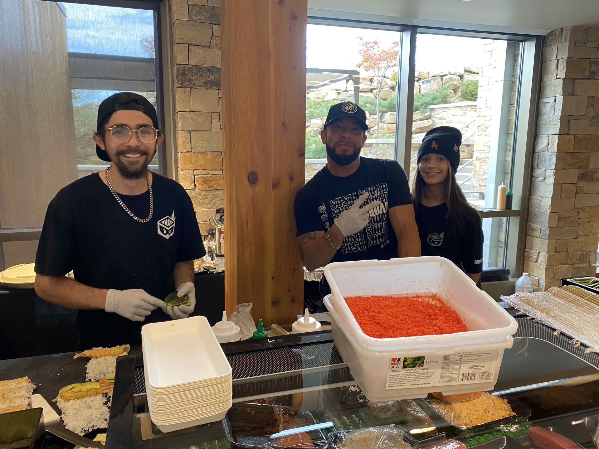 A group of people are standing around a counter making sushi.