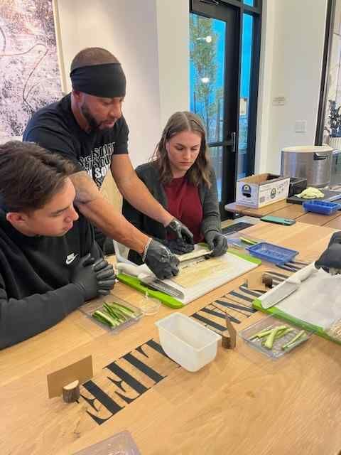 A group of people are sitting at a table cutting vegetables.