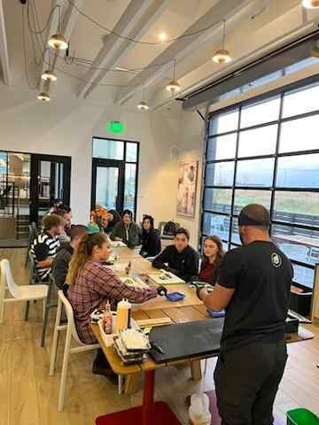 A sushi chef is standing in front of a group of people sitting at tables in a room.