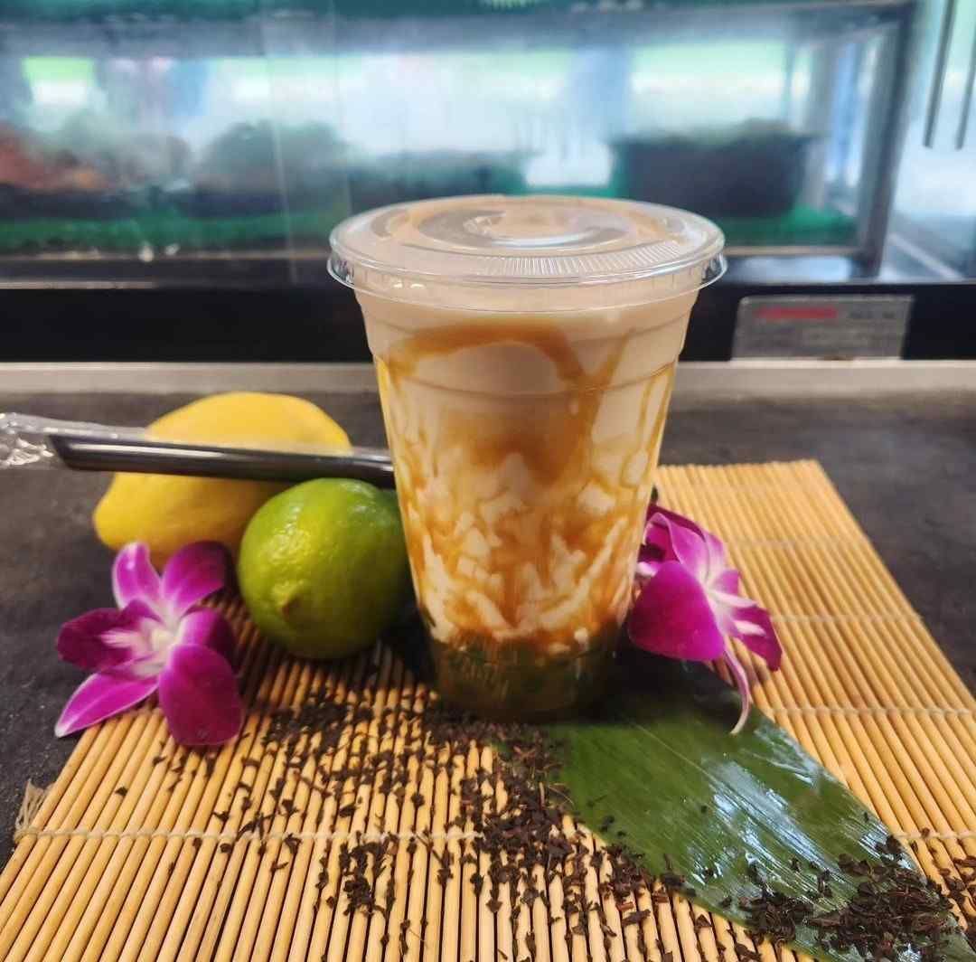 A cup of liquid is sitting on a bamboo mat next to lemons and flowers.