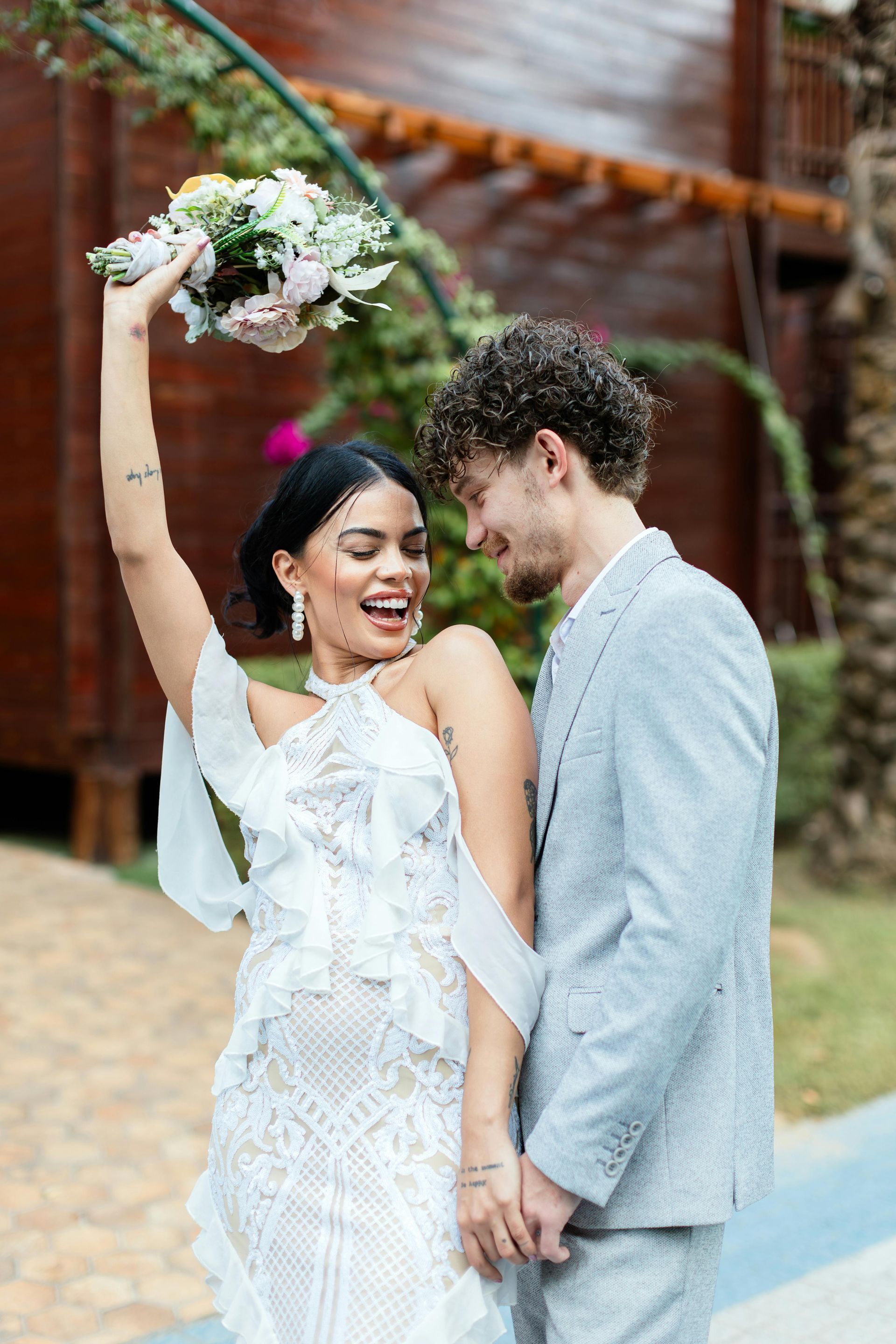 A bride and groom are standing next to each other and the bride is holding a bouquet of flowers in the air.