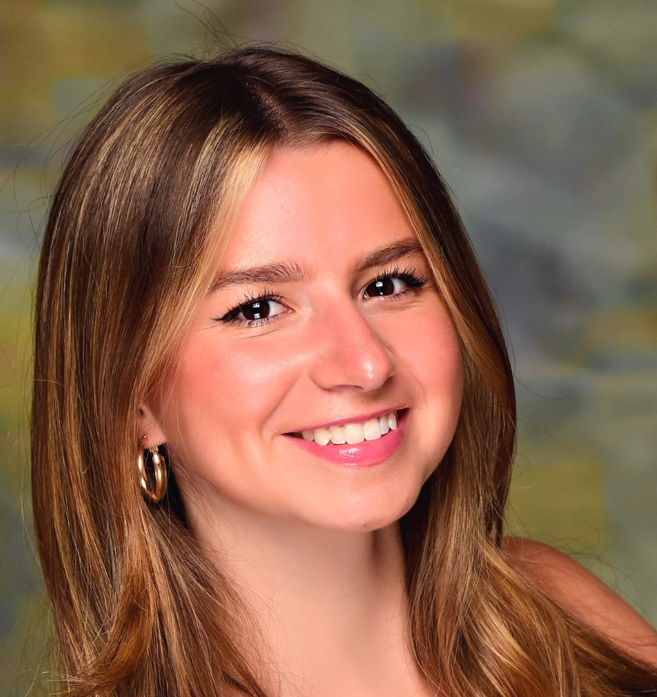 Woman with long, light brown hair smiles at the camera, wearing gold hoop earrings.