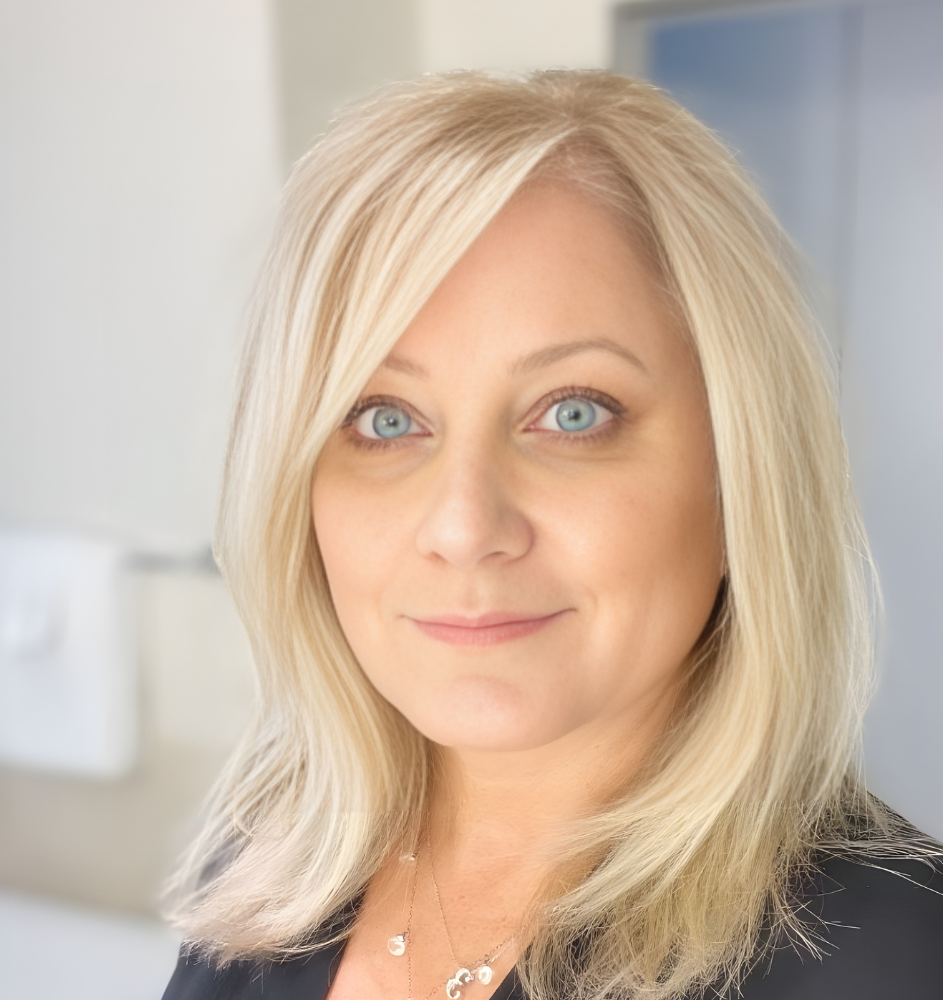 Blonde woman with blue eyes smiles, close-up portrait. Light-colored hair, wearing a black shirt.