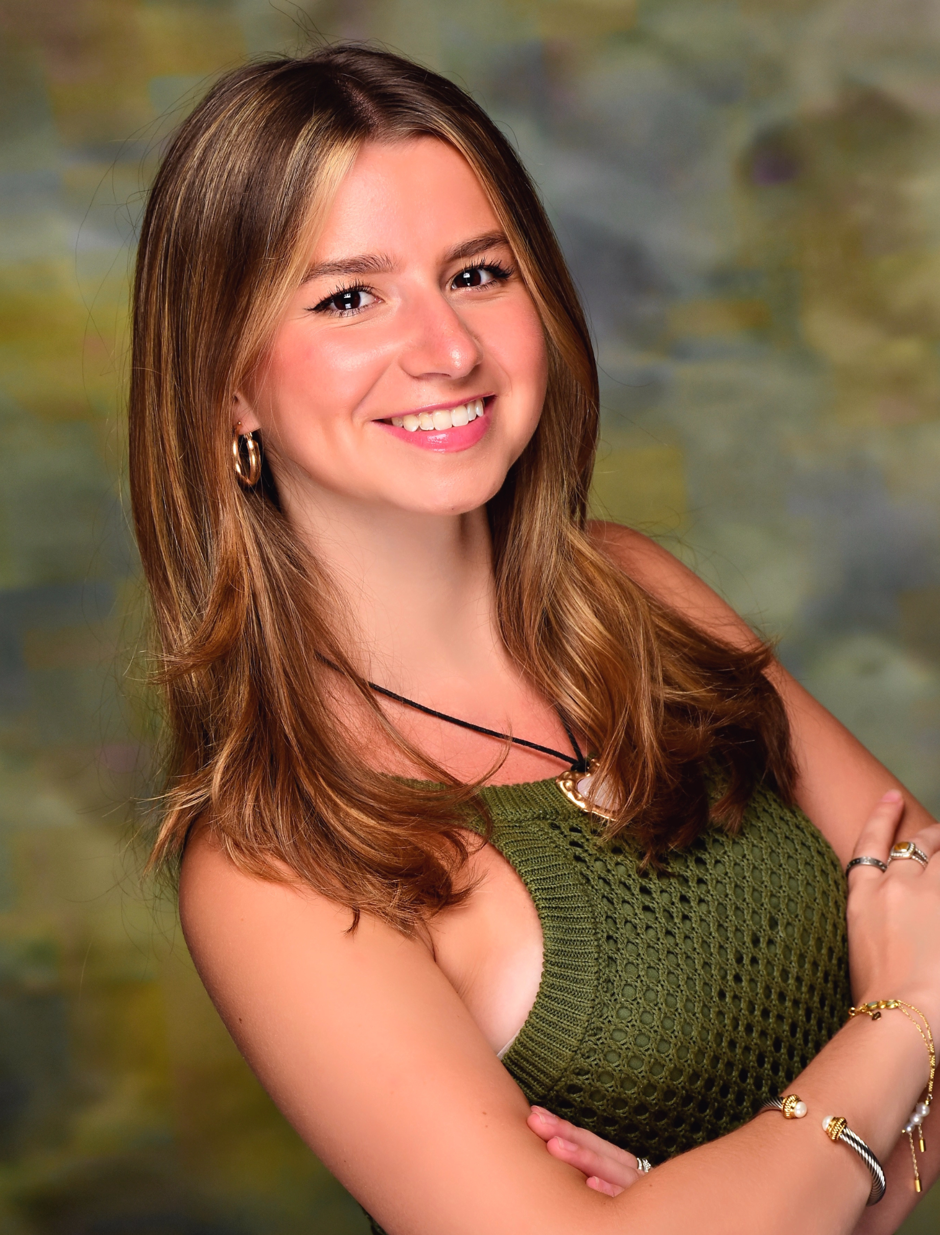 Woman with long, light brown hair smiles, wearing a green top, posing with arms crossed.