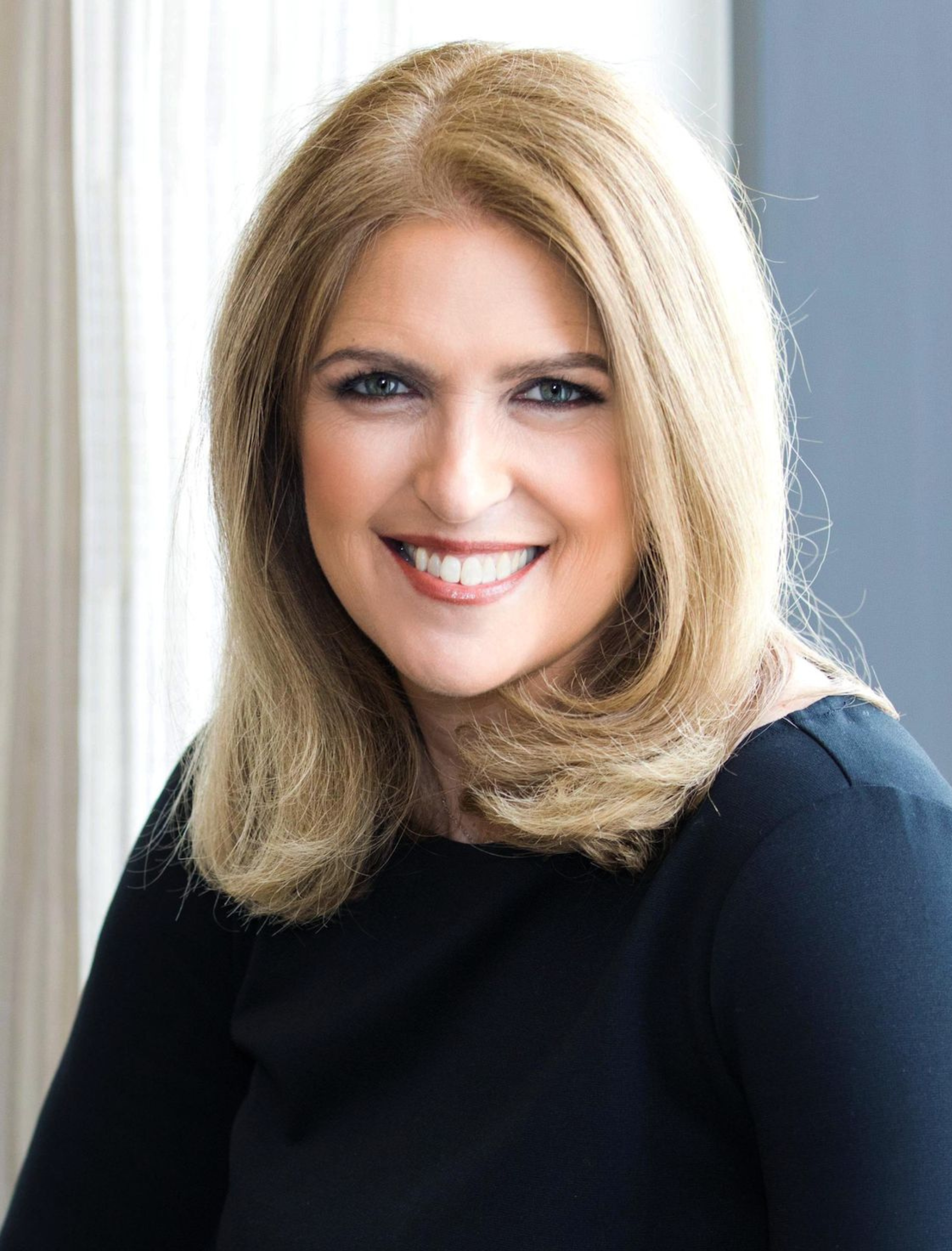 Woman with blonde hair, smiling, wearing a black top.