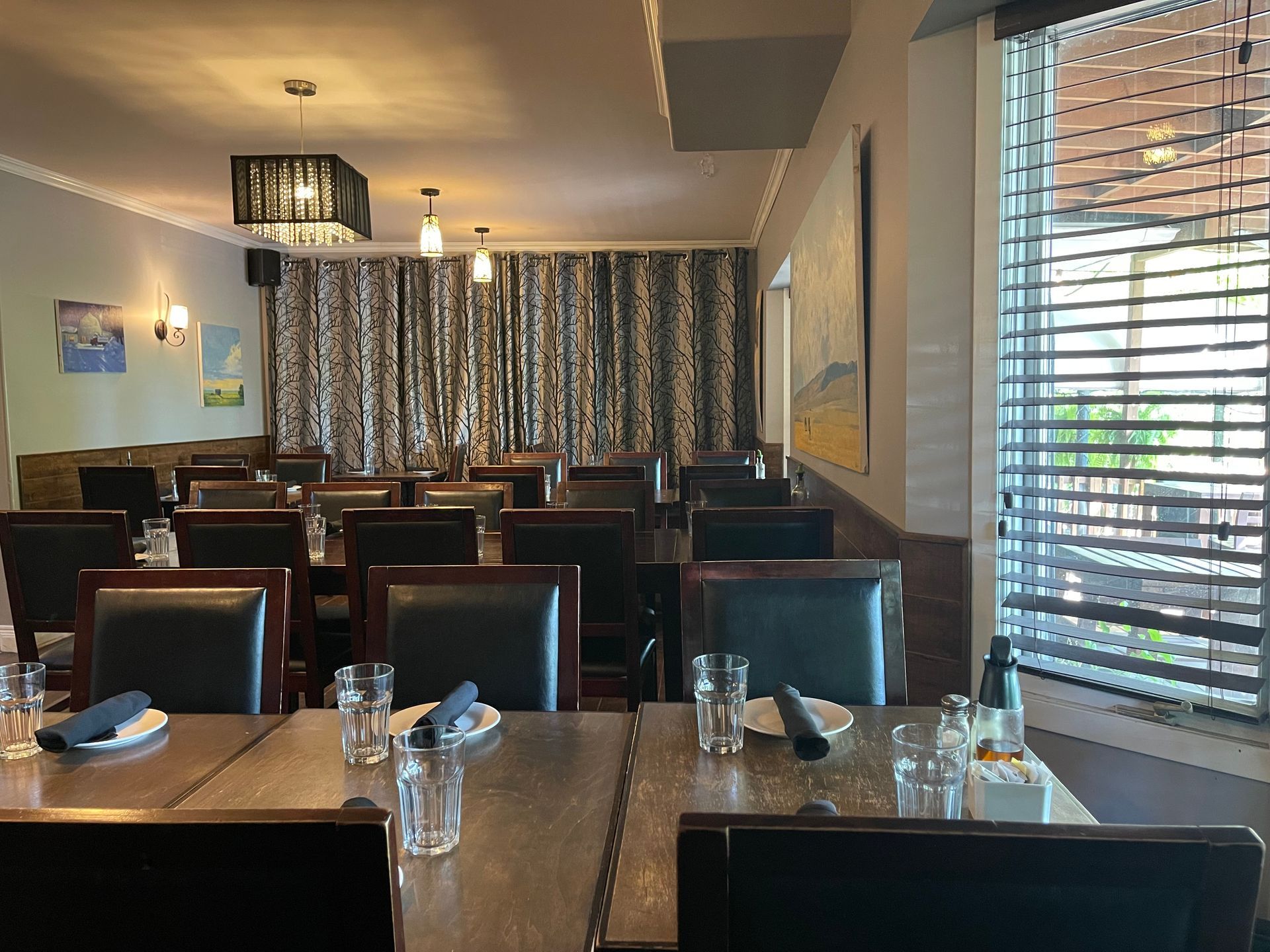 Restaurant dining tables set with glassware and chairs, under a chandelier.