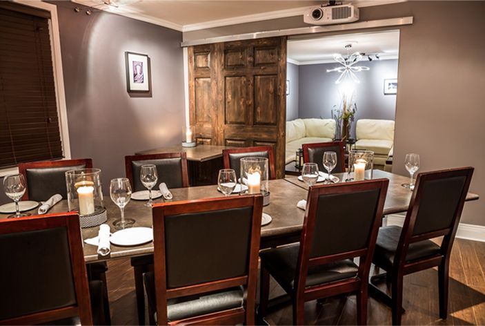 A dining room with a long table set for a meal, adjacent to a living room, brown tones and gray walls.
