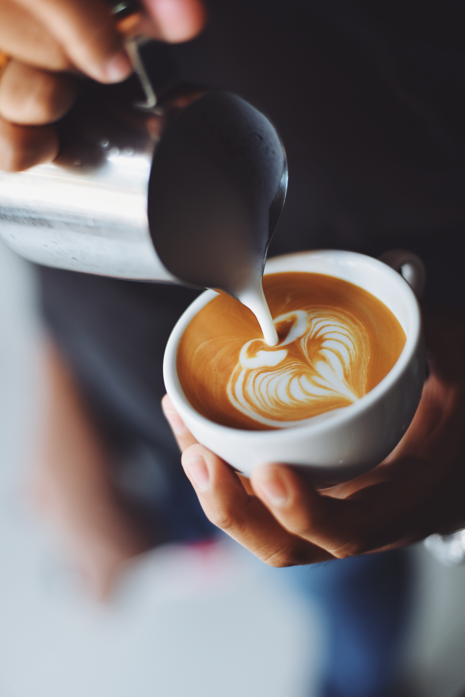Barista pouring steamed milk into a coffee cup, creating a latte art heart.