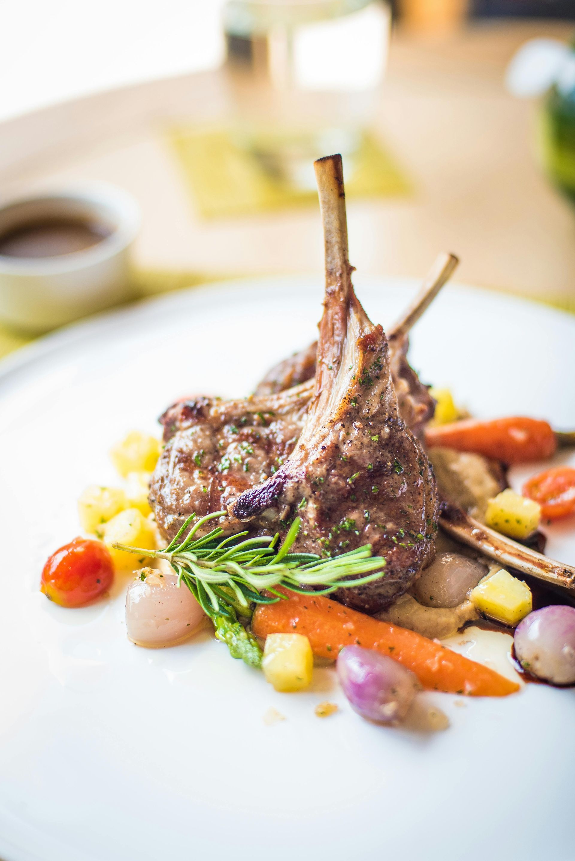 Rack of lamb with roasted vegetables on a white plate, presented in a restaurant setting.