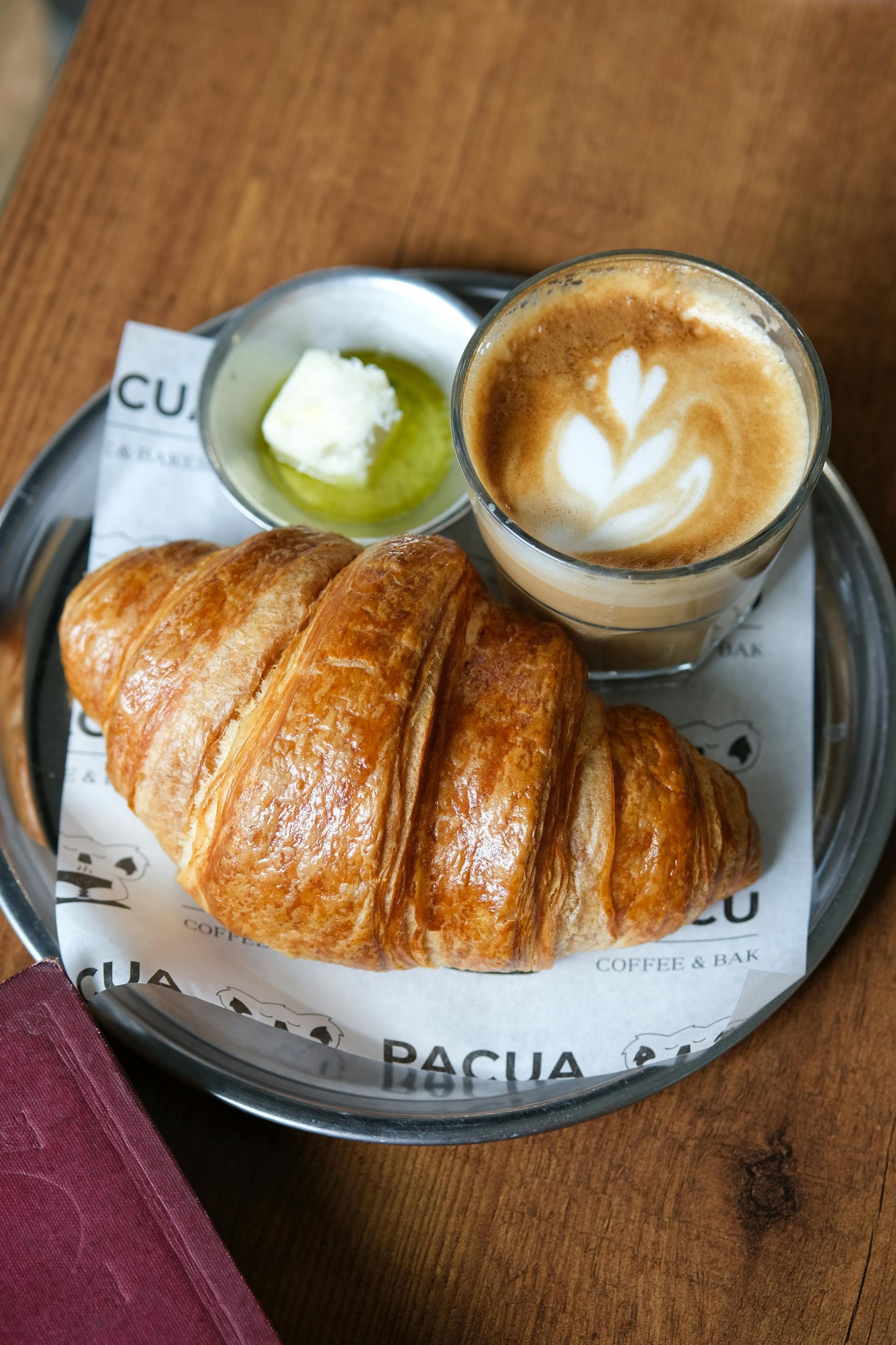 Outdoor cafe with tables and chairs, beneath a striped awning. A person sits at a table, and a street runs alongside.
