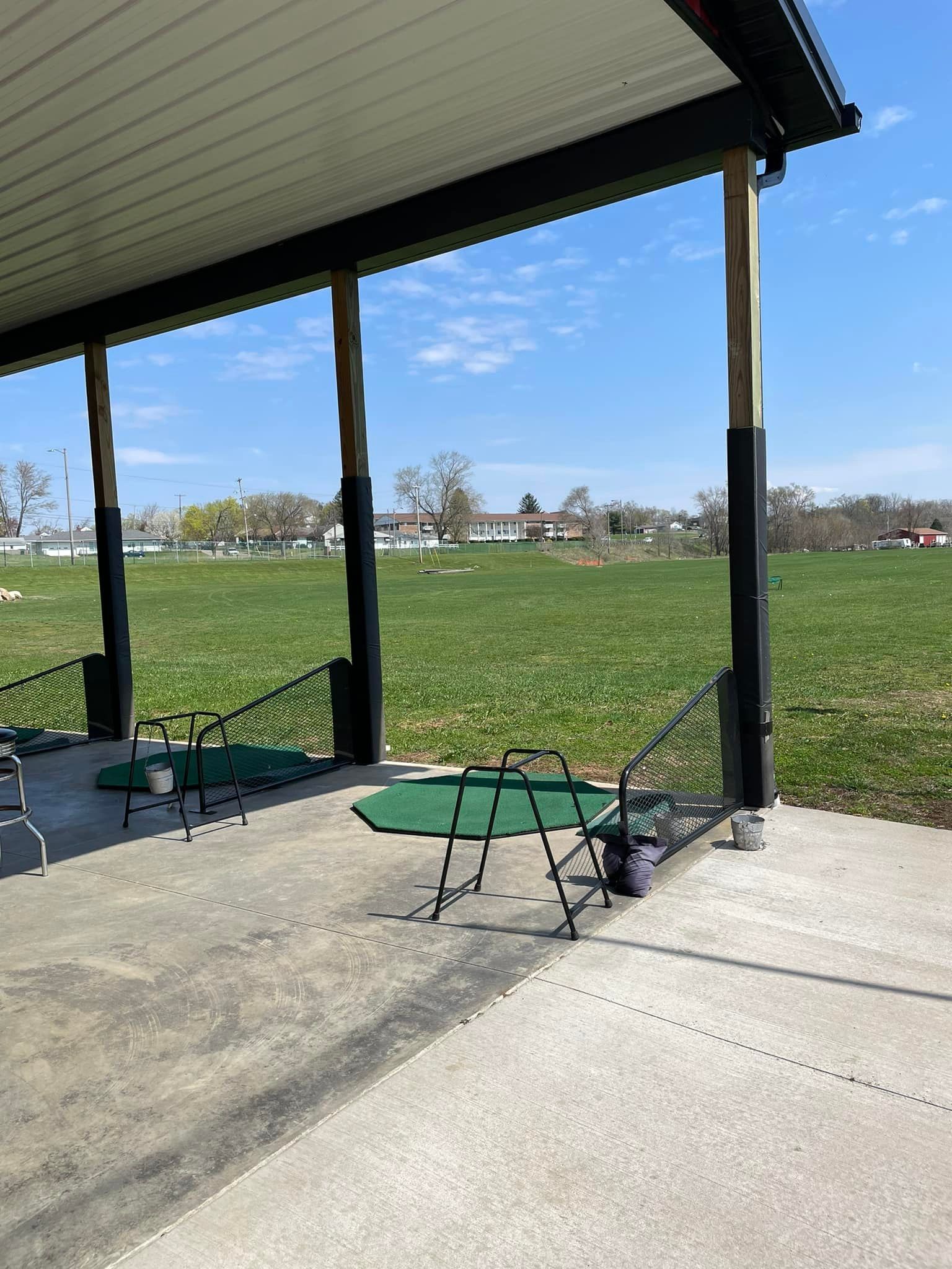 A covered area with a table and chairs in front of a grassy field.