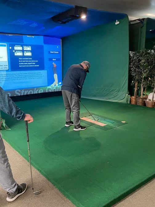 A man is playing golf in a simulator while holding a golf club.