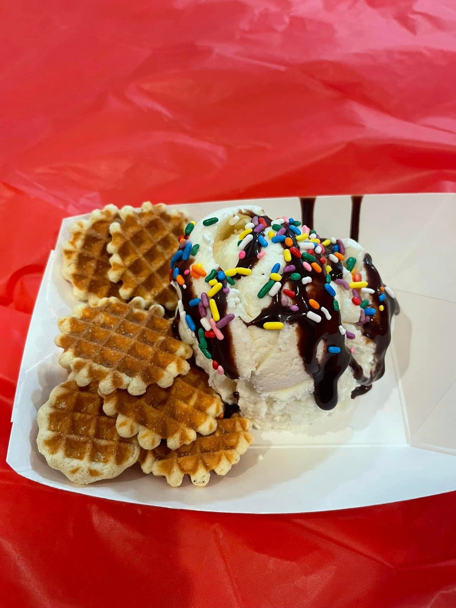 A paper plate topped with ice cream , waffles and sprinkles.