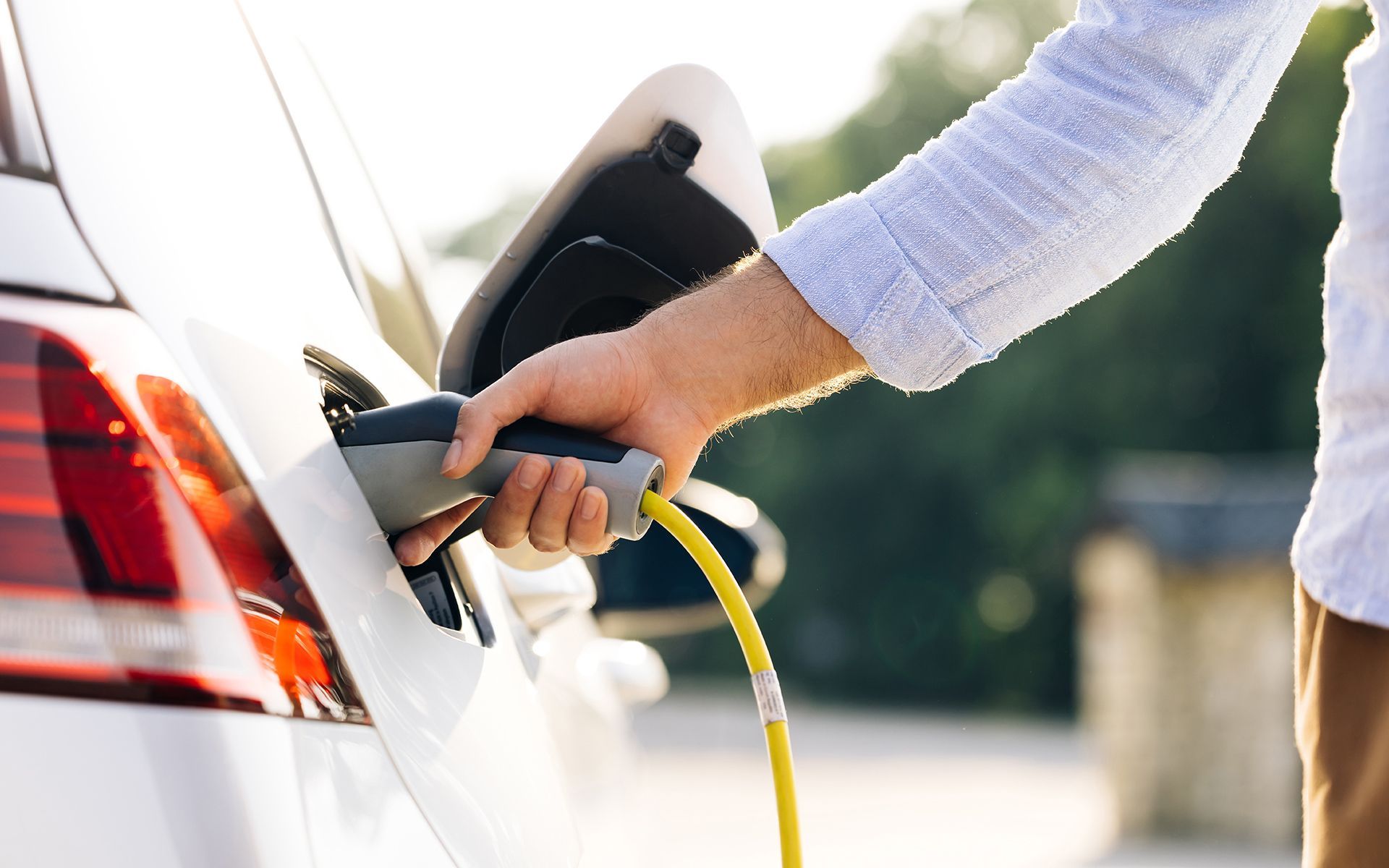 Person plugging an electric car charger into a white car's charging port.