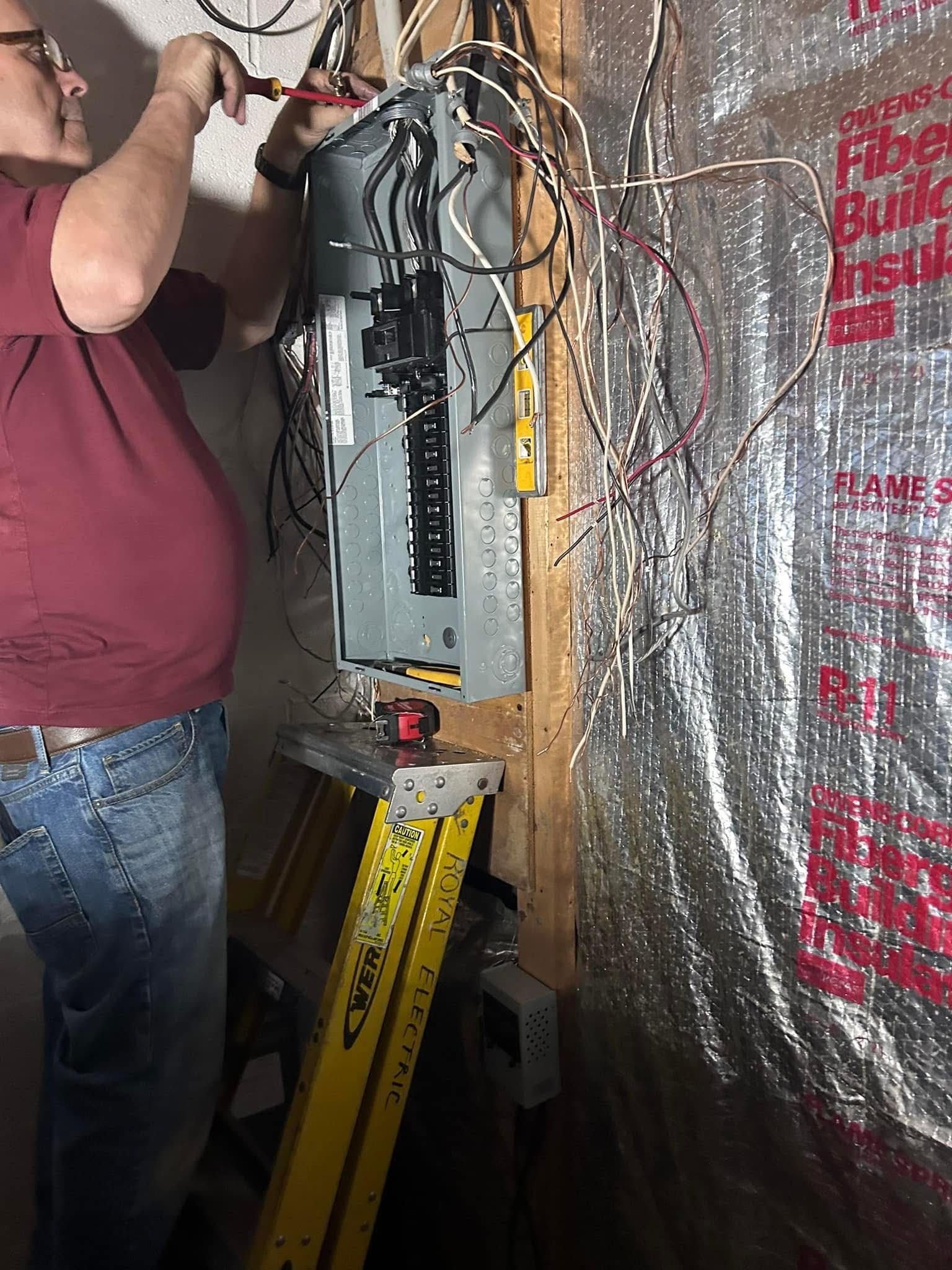 A person works on an electrical panel with tools. Indoors, near insulated wall.