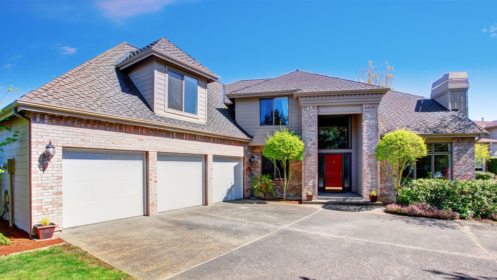 Two-story brick house with three-car garage, red front door, and blue sky.