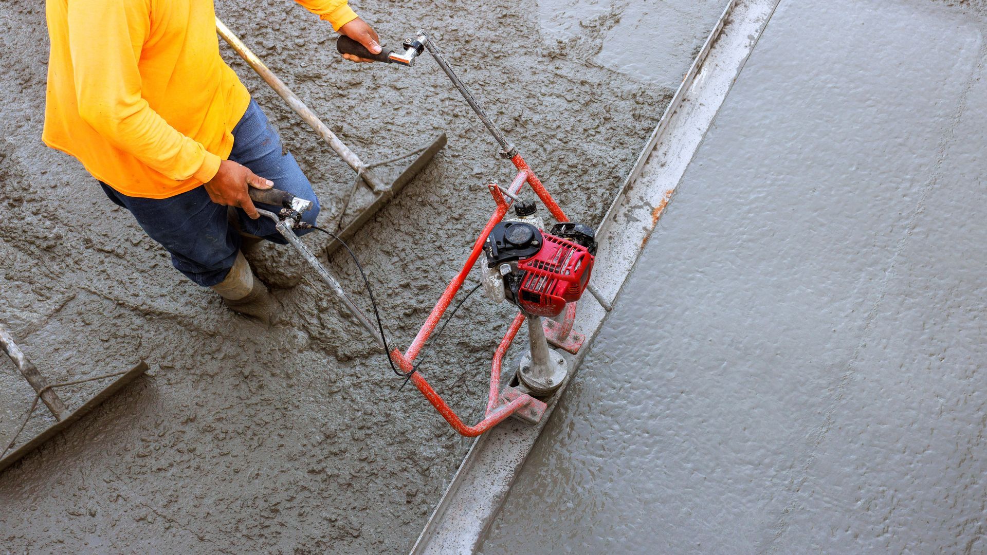 Person smoothing wet concrete with a power screed in a construction setting.