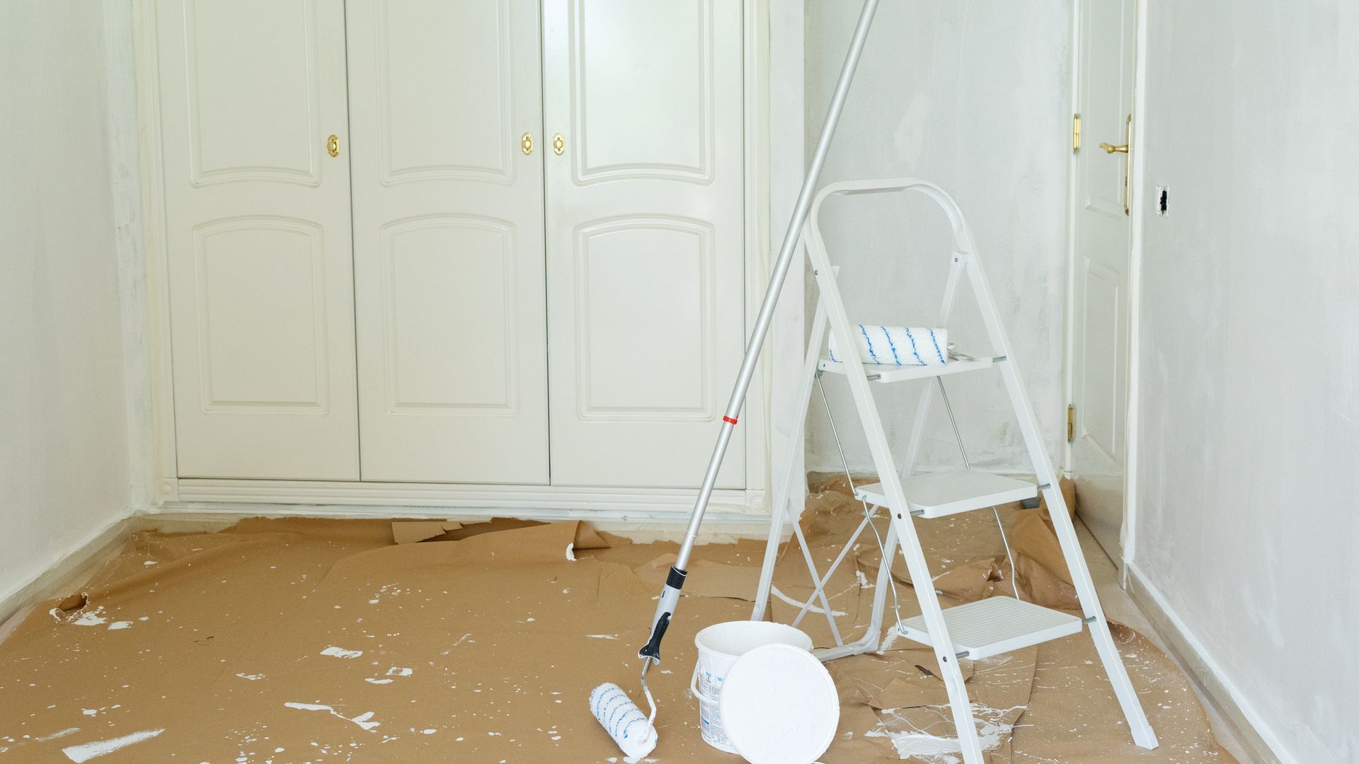 Room being painted, with a ladder, paint roller, and paint bucket.