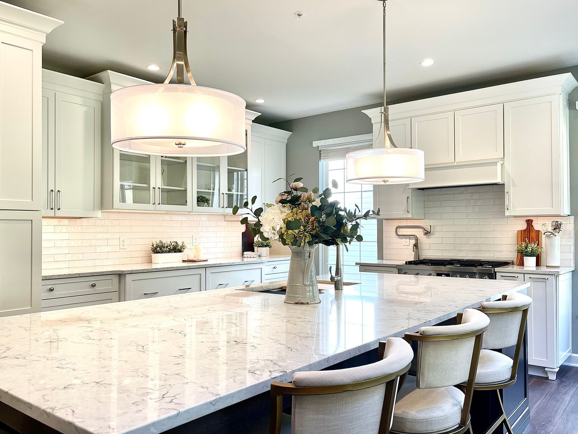 A kitchen with white cabinets and a large island with a vase of flowers on it.