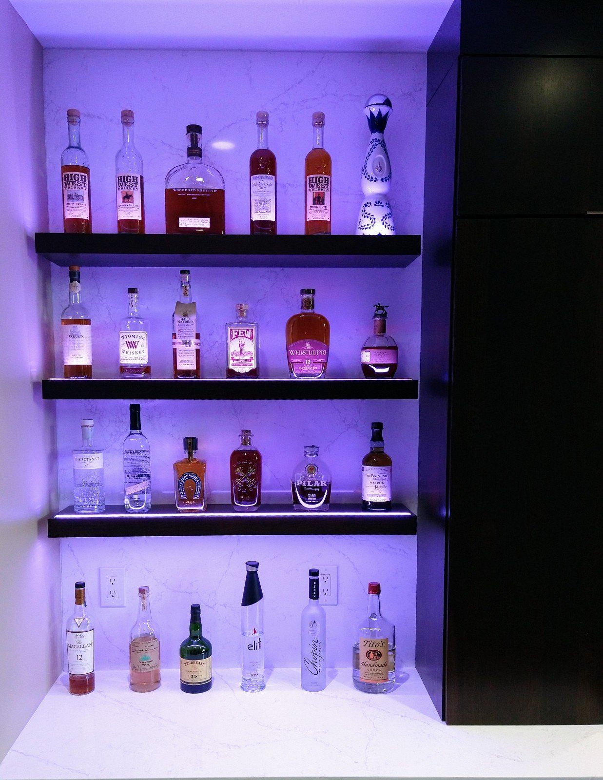 Several bottles of liquor are displayed on shelves with purple lights
