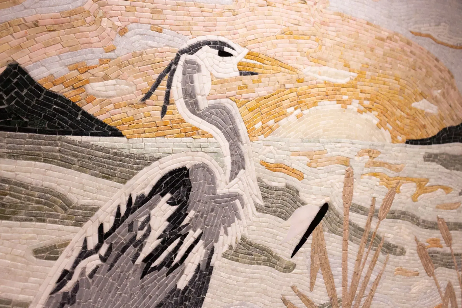 A mosaic of a heron standing next to a body of water.