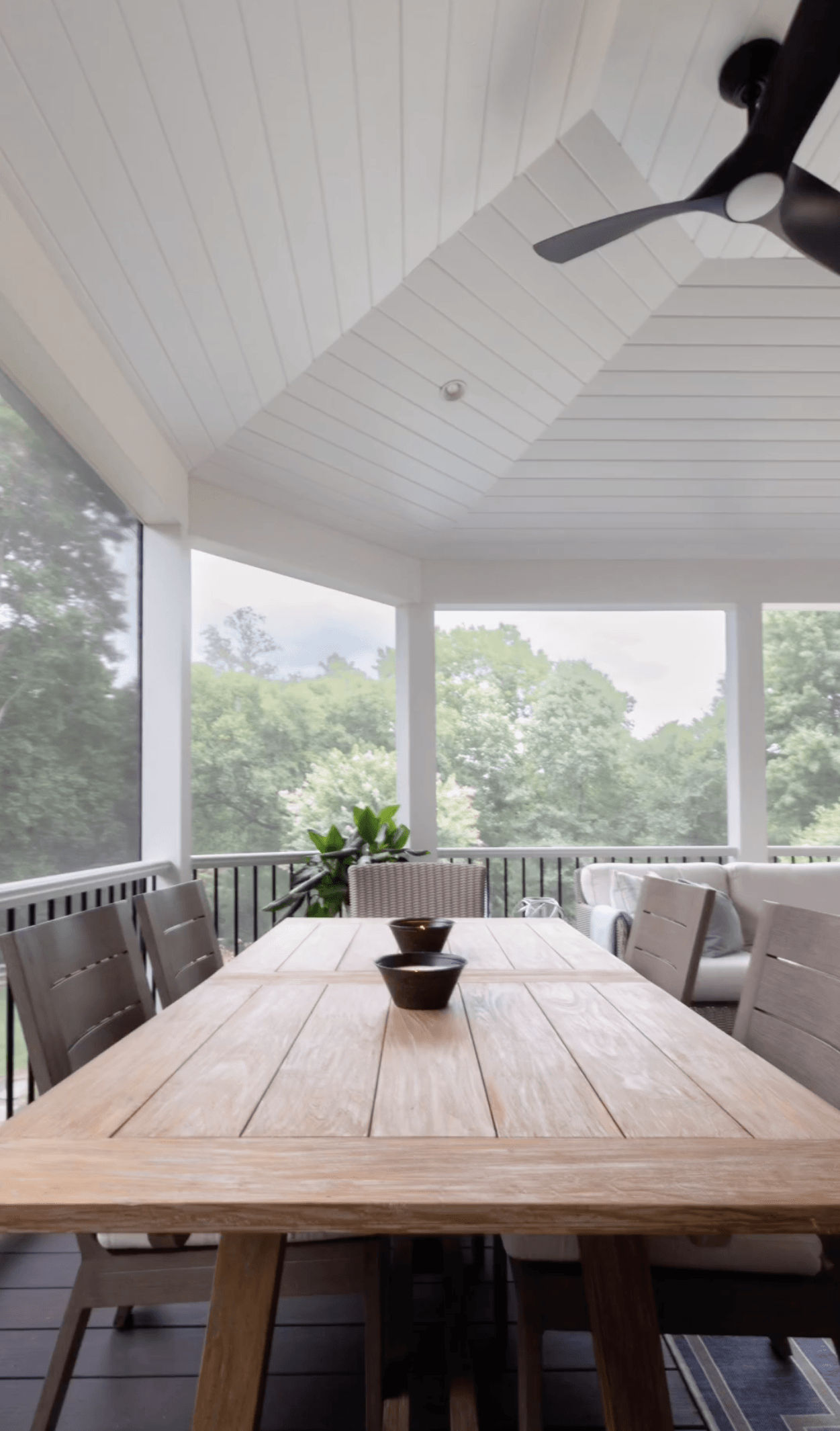 A screened in porch with a wooden table and chairs and a ceiling fan.